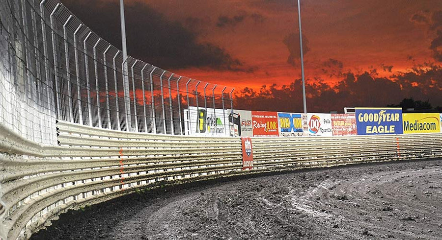 Dirt-track corner, safety fence, and sunset sky.